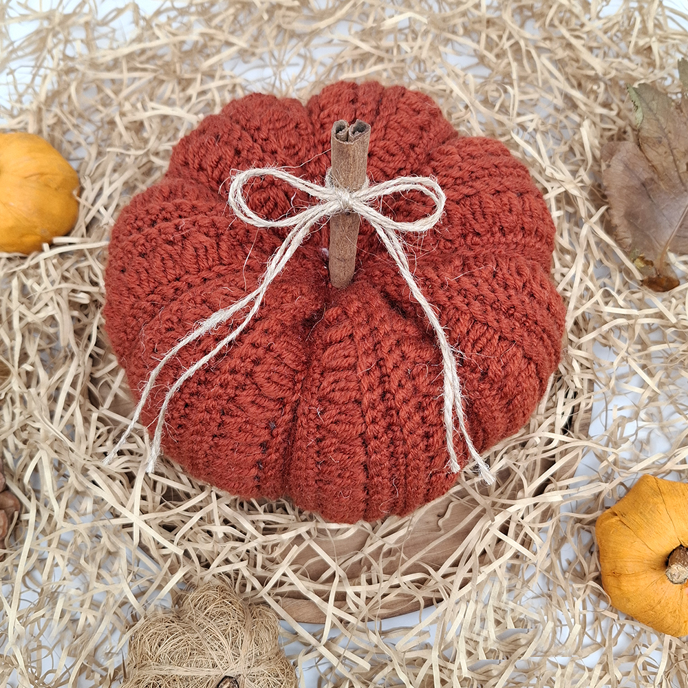 Knitted pumpkin decoration with twine on a straw background