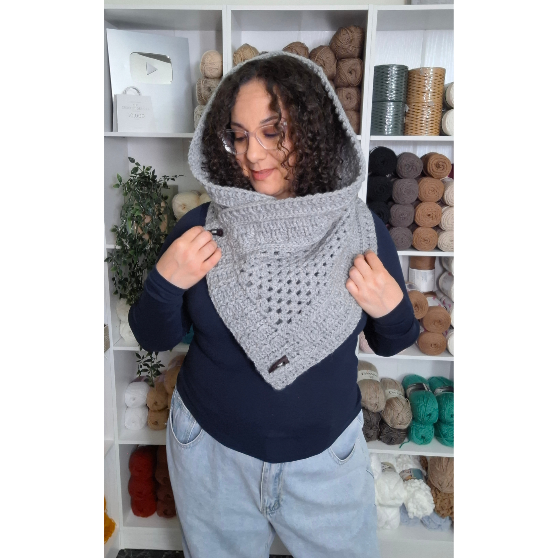 A woman wearing a gray crocheted hooded cowl neck warmer over a navy blue top and light wash jeans.